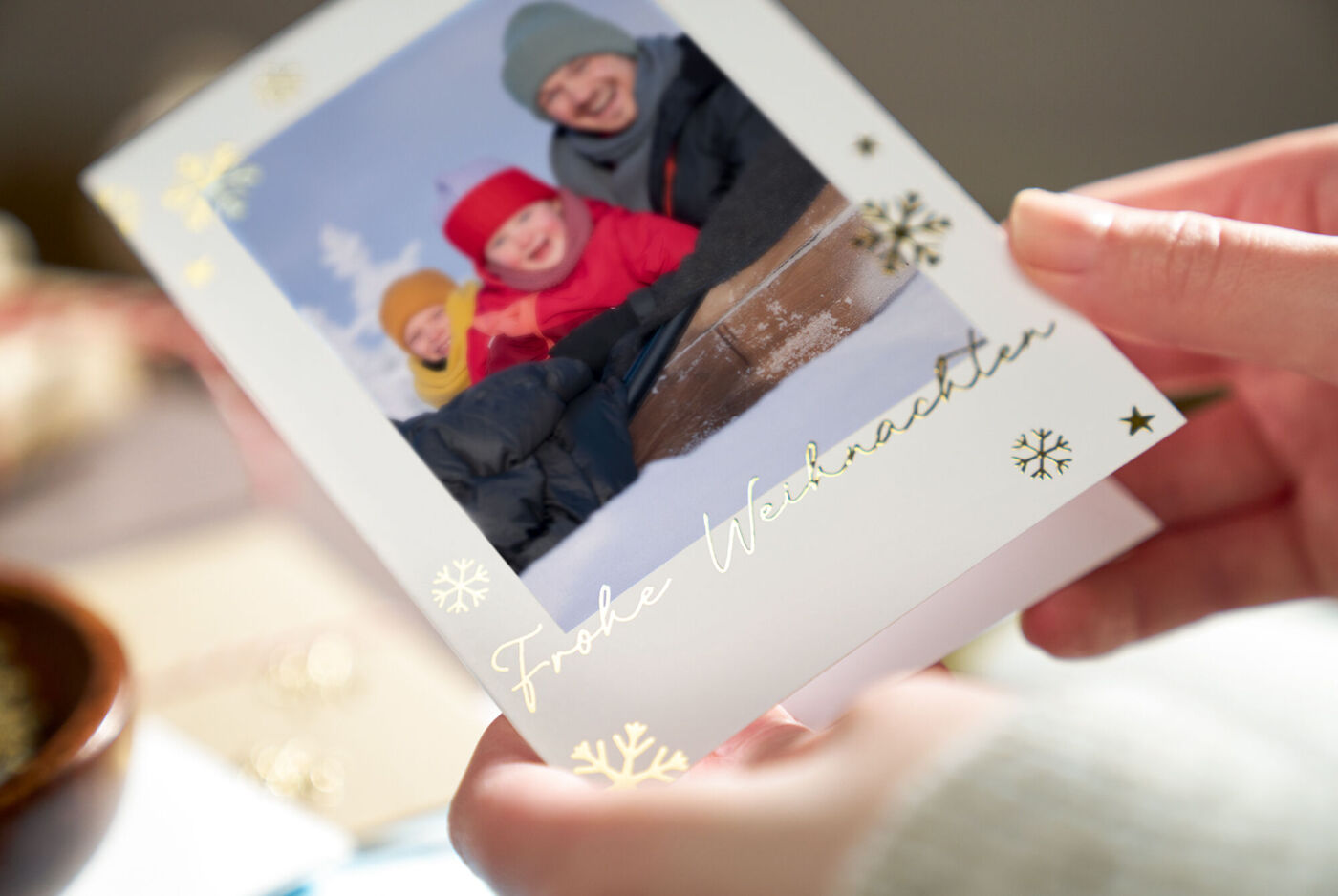 Eine Person hält eine festliche Grußkarte mit Weihnachtsmotiv und Kindern in Winterkleidung.
