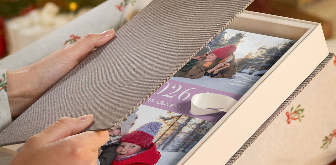 Eine Person öffnet eine Geschenkbox mit einem CEWE FOTOBUCH.