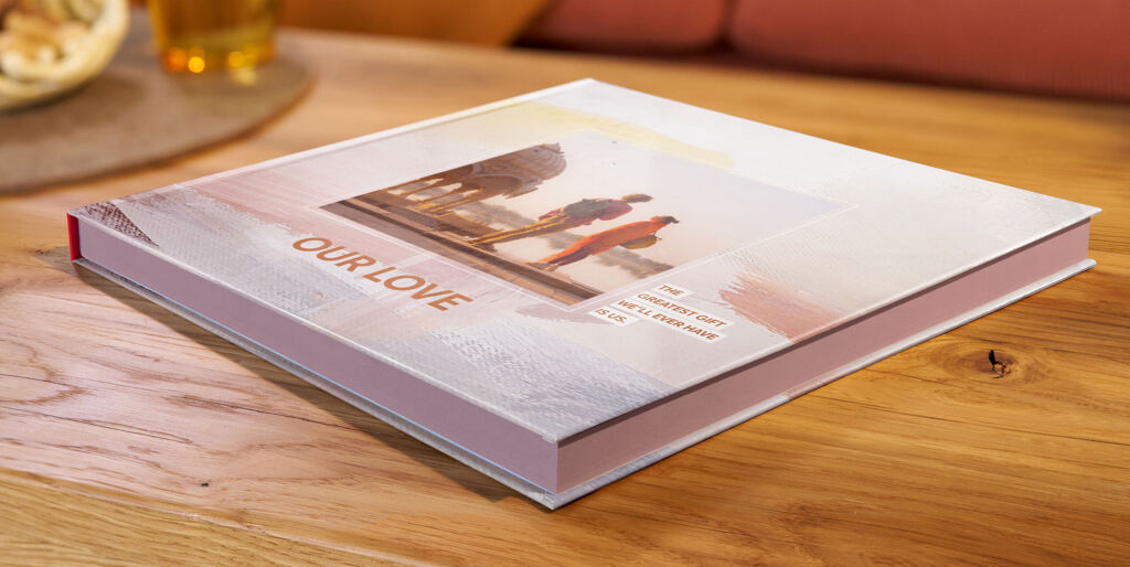 Auf einem Couchtisch liegt ein CEWE FOTOBUCH mit Farbschnitt, das Cover zeigt drei Foto von einem lachenden Pärchen.