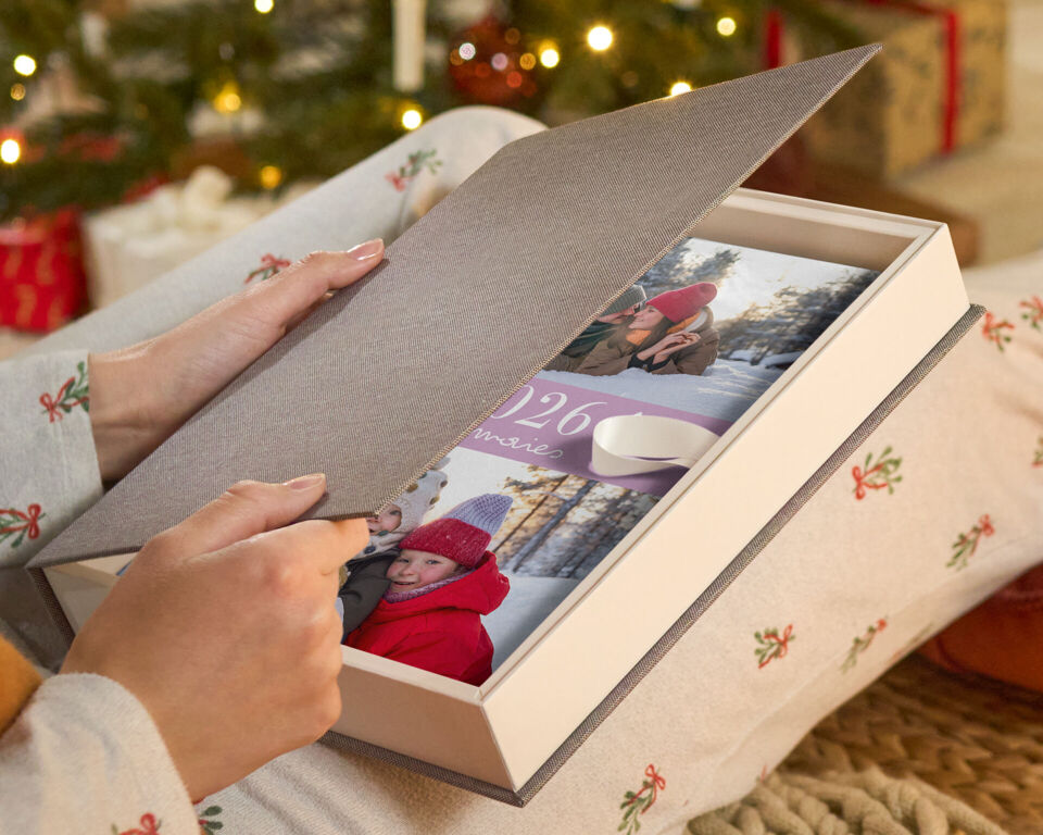 Eine Person öffnet eine Geschenkbox mit einem CEWE FOTOBUCH mit Winterfotos.