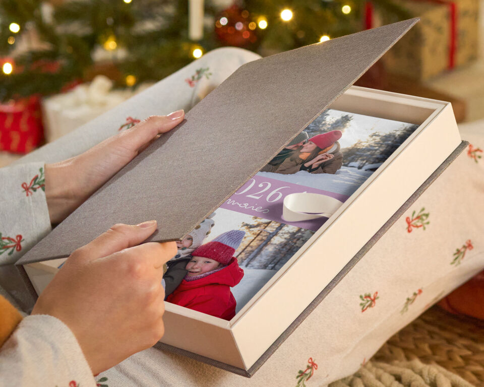 Eine Person öffnet eine Geschenkbox mit einem CEWE FOTOBUCH.