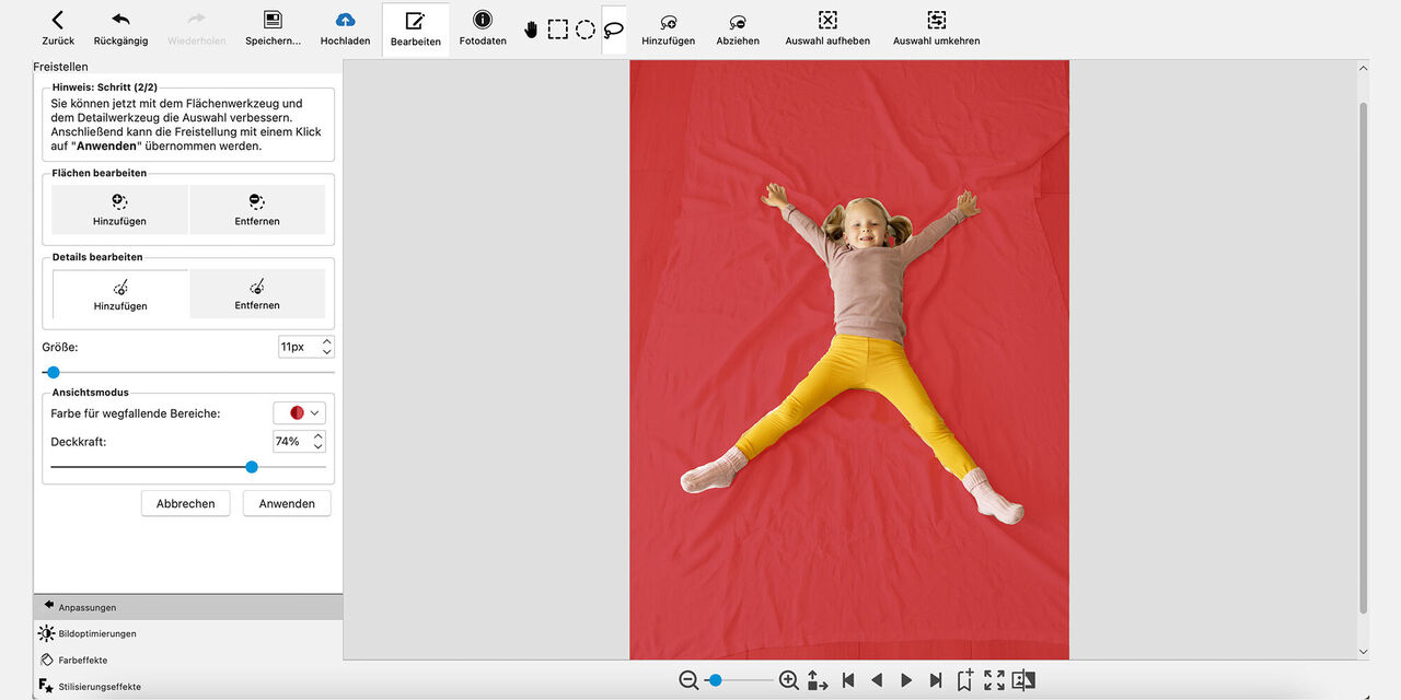 Screenshot der CEWE Fotowelt Software: Es ist ein Mädchen zu sehen, das auf dem Boden auf einer ausgebreiteten Decke liegt und in die Kamera lächelt. Beide Arme und Beine hat es dabei weit von sich gestreckt. Der Untergrund, auf dem das Mädchen liegt, ist rot eingefärbt.